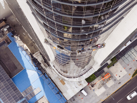 Aerial view of construction workers on a suspended scaffold platform cleaning the glass facade of a modern skyscraper in Santo Domingo, Dominican Republic.