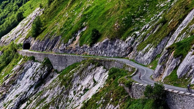 Aerial view of the winding Col d'Aubisque mountain road with cyclists riding along the steep rocky slopes in Beost, Nouvelle-Aquitaine, France.