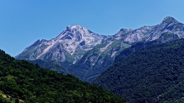 Aerial view of the rugged peaks of Col d'Aubisque, featuring steep rocky slopes, dense green forests, and clear blue sky in Beost, Nouvelle-Aquitaine, France.