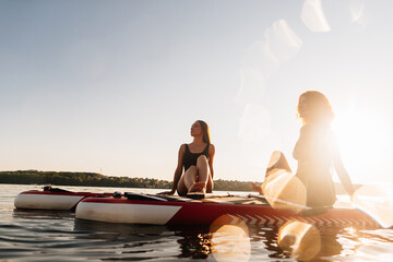 Fototapeta premium Women paddleboarding relaxing on water at sunset