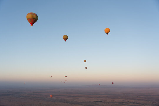 View of multiple colorful hot air balloons floating over the vast desert landscape at sunrise near Marrakesh, Marrakesh-Safi, Morocco.