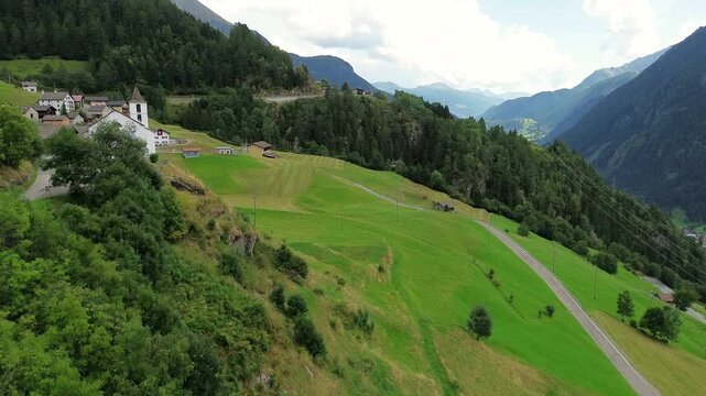 Aerial view of a historic church perched on a green hillside with a winding road and lush forest in Quinto di Treviso, Veneto, Italy.