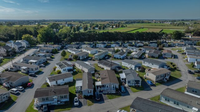 Aerial view of a residential mobile home park with rows of houses, paved streets, parked cars, and surrounding green fields in the USA.