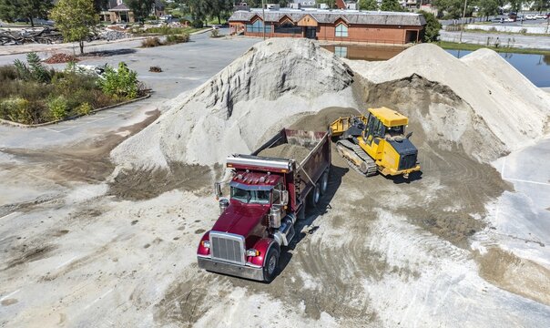 Aerial view of a red dump truck and a yellow bulldozer working at a construction site with large piles of sand in the USA.