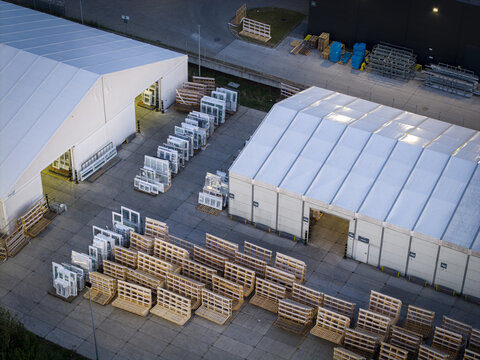 Aerial view of a logistics facility featuring large white tent warehouses, rows of wooden pallets, and window frames stored on the concrete yard in Krakow, Lesser Poland Voivode, Poland.