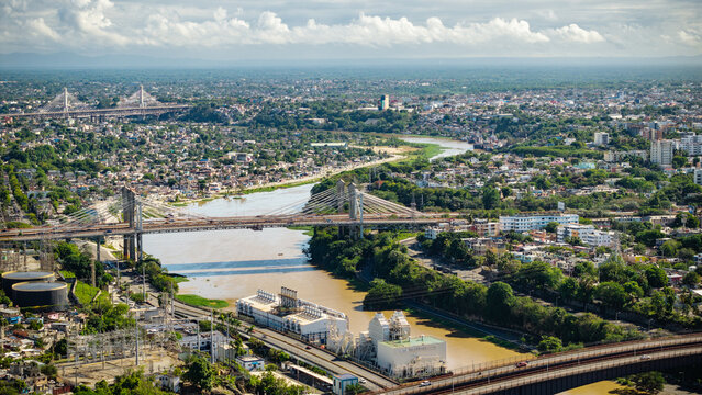 Aerial view of Rio Ozama flowing through the urban landscape of Santo Domingo, featuring cable-stayed bridges and dense residential areas in Santo Domingo, DN, Dominican Republic.
