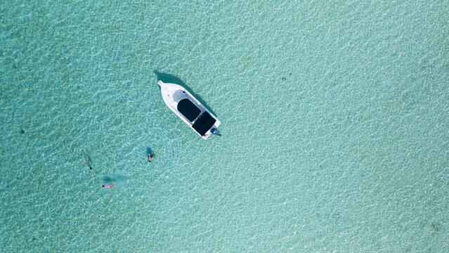 Aerial view of a small motorboat floating in crystal clear turquoise water with people swimming nearby in Spanish Wells, The Bahamas.