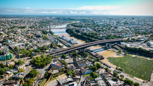 Aerial view of Rio Ozama flowing through the urban landscape with bridges, industrial buildings, and dense city streets Santo Domingo, DN, Dominican Republic.