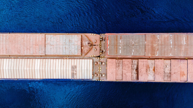Aerial view of a large cargo ship with weathered reddish-brown hatches sailing on deep blue sea in Greece.