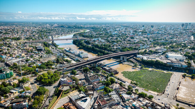Aerial view of Rio Ozama flowing through the urban landscape with bridges, dense buildings, and green trees in Santo Domingo, DN, Dominican Republic.
