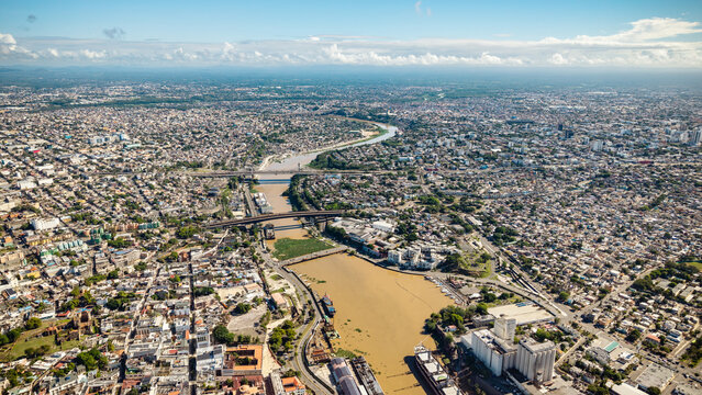 Aerial view of Rio Ozama winding through the dense urban landscape with bridges spanning the river and ships docked along the banks in Santo Domingo, DN, Dominican Republic.