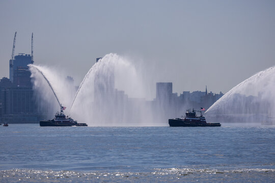 Jersey City, New Jersey, United States - 04 July 2026: View of two tugboats performing a water display in the harbor with the city skyline in the background.