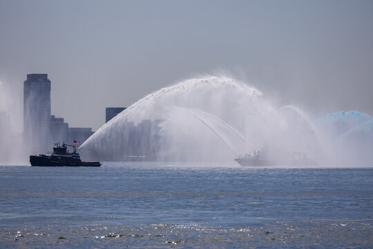 Jersey City, New Jersey, United States - 04 July 2026: View of a tugboat performing a water display in the harbor near Liberty State Park with the city skyline in the background.