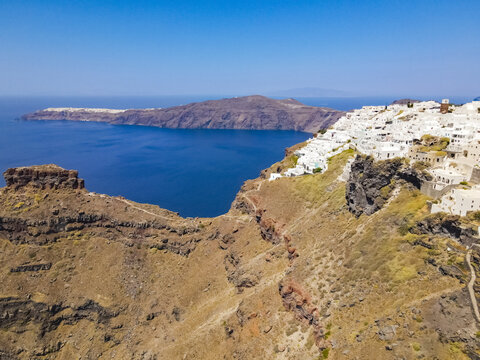 Aerial view of the white buildings of Fira perched on the volcanic caldera cliffs overlooking the deep blue Aegean Sea in Fira, Greece.