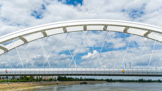 Aerial view of Zezelj Bridge spanning the Danube River with its distinctive white steel arch structure against a blue sky with clouds in Novi Sad, Vojvodina, Serbia.