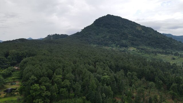 Aerial view of lush green forested mountains and rolling hills under a cloudy sky in Babakan Madang, West Java, Indonesia.