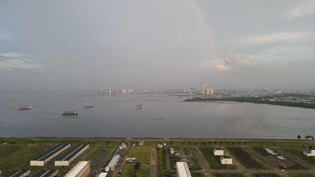 Aerial view of Golf Island in PIK with modern residential buildings, calm sea, and a faint rainbow in the sky in Kecamatan Penjaringan, Daerah Khusus Ibukota, Indonesia.