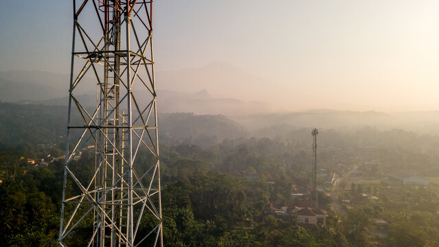 Aerial view of a telecommunications tower rising above the misty landscape and lush greenery of Keniten in Kedungbanteng, Central Java, Indonesia.