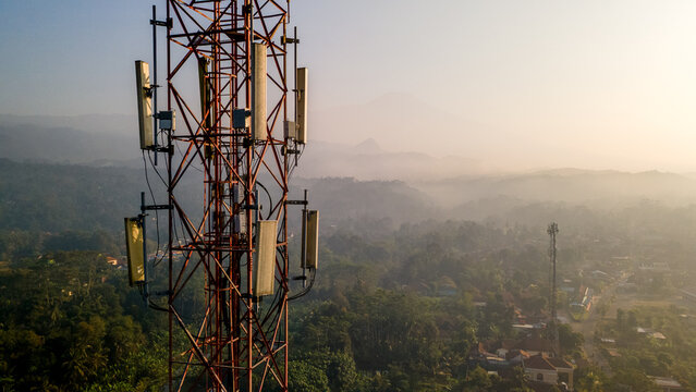 Aerial view of a tall telecommunications tower rising above a lush, misty landscape with dense trees and distant hills in Kedungbanteng, Central Java, Indonesia.