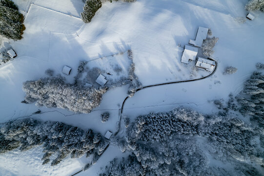Aerial view of Dienersberger Weg with snow-covered farmhouses, winding paths, and dense pine forests in the winter landscape of Oberstdorf, Bayern, Germany.