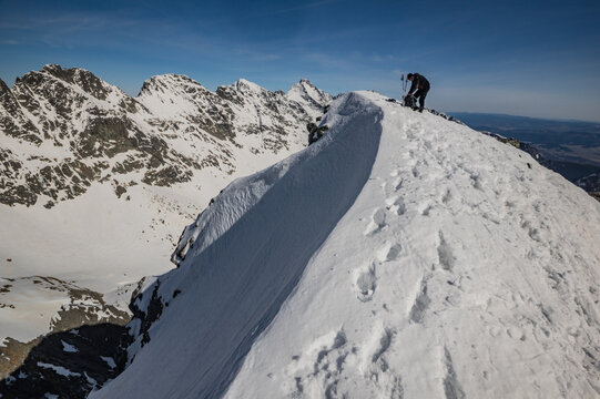 Vysoke Tatry, Slovakia - 02 April 2025: View of a climber on the snowy ridge of Koprovsky stit in the High Tatras national park with rugged mountain peaks under a clear blue sky.
