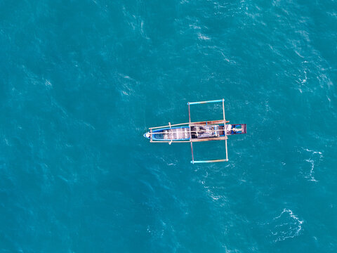 Aerial view of a traditional outrigger boat floating on the turquoise waters of Pantai Legon Pari in Kecamatan Bayah, Banten, Indonesia.