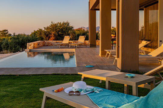 View of a luxury villa patio with an infinity pool, sun loungers, and olive trees at sunset in Chania, Greece.