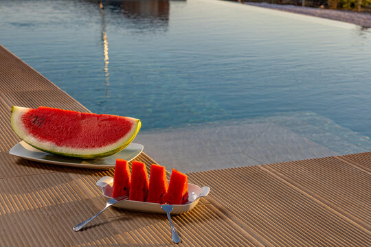 View of fresh watermelon slices served on a plate by a swimming pool on a sunny day in Chania, Greece.