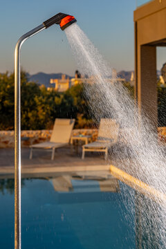 View of an outdoor shower spraying water by a swimming pool with lounge chairs in the background, Chania, Greece.