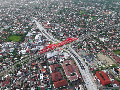 Aerial view of Jembatan Kereta Api Joglo with its distinctive red steel structure spanning over the urban landscape of Kecamatan Banjarsari, Jawa Tengah, Indonesia.