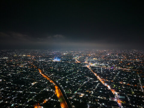 Aerial view of Jembatan Kereta Api Joglo illuminated at night amidst the sprawling city lights of Surakarta in Kecamatan Banjarsari, Jawa Tengah, Indonesia.