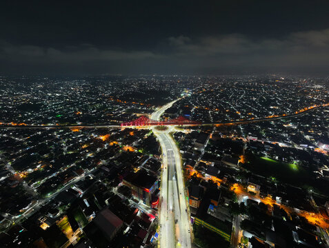 Aerial view of the illuminated Jembatan Kereta Api Joglo spanning across the urban landscape with glowing city lights and road networks at night in Kecamatan Banjarsari, Jawa Tengah, Indonesia.