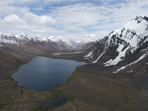 Aerial view of Karambar Lake surrounded by snow-capped mountains and rugged terrain in Pakistan.