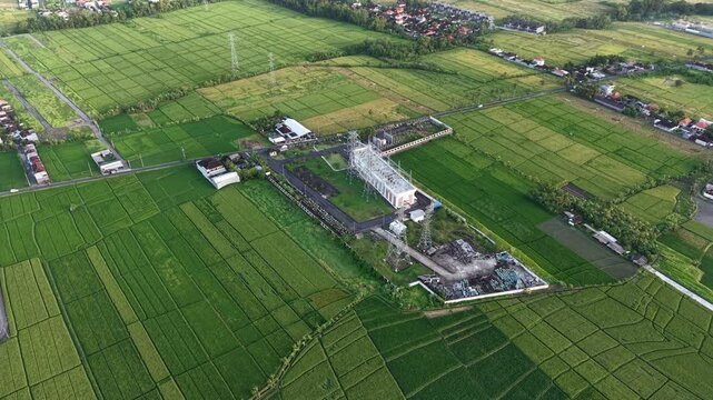 Aerial view of electrical substation surrounded by lush green rice fields in Kecamatan Kediri, Bali, Indonesia.