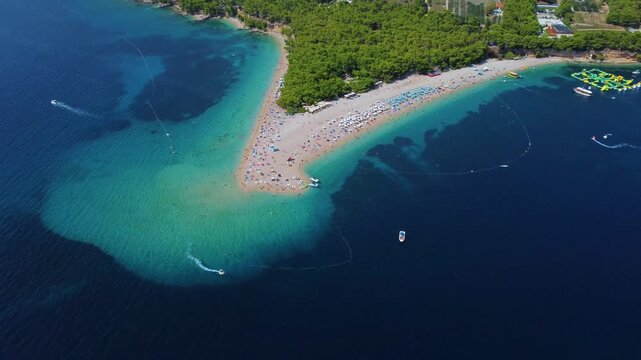 Aerial view of the iconic Golden Horn Beach with turquoise waters, pine forests, and beachgoers in Bol, Split-Dalmatia County, Croatia.