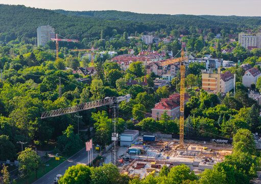 Aerial view of a construction site with tall yellow cranes surrounded by lush green trees and residential buildings in Sopot, Pomeranian Voivodeship, Poland.