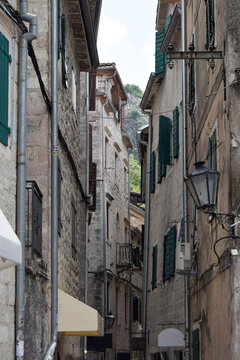 View of a narrow alleyway in the historic Old Town of Kotor with stone buildings, green shutters, and hanging lanterns in Kotor, Kotor Municipality, Montenegro.