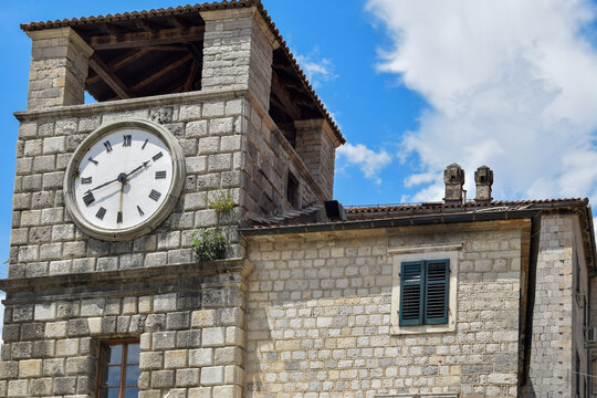 View of the historic Clock Tower with its stone masonry and Roman numeral clock face set against a bright blue sky in Kotor, Kotor Municipality, Montenegro.