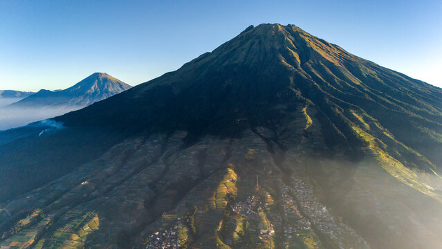 Aerial view of Nepal Van Java village nestled on the slopes of Mount Sumbing with terraced vegetable fields and morning mist in Kecamatan Kaliangkrik, Jawa Tengah, Indonesia.