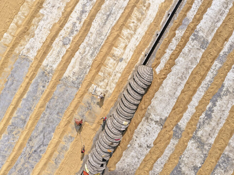 Brahmanbaria, Bangladesh - 24 January 2026: Aerial view of Ashuganj grain drying area with workers spreading rice on concrete strips and a row of conical hats.