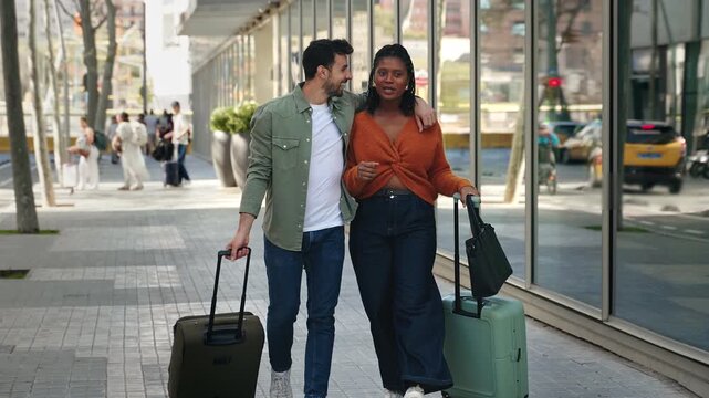 Smiling tourist couple walking with luggage, bonding during romantic vacations trip 