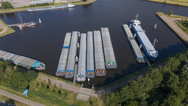 Aerial view of the Wachthaven featuring several cargo barges moored in the calm harbor waters surrounded by lush green trees and rural landscape in Staphorst, Overijssel, Netherlands.