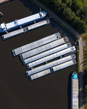 Aerial view of cargo barges moored in the Wachthaven harbor, surrounded by green trees and calm water in Staphorst, Overijssel, Netherlands.