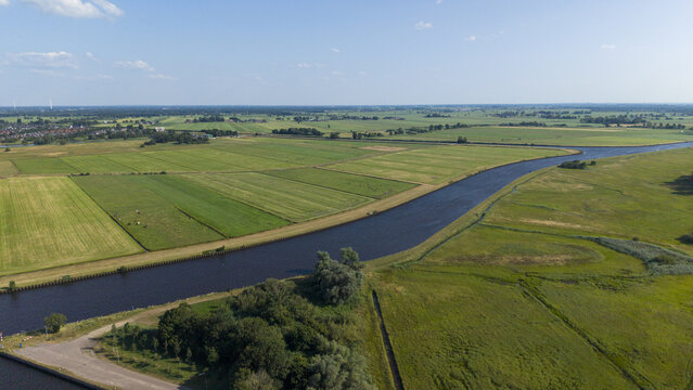 Aerial view of the canal winding through the lush green agricultural fields and meadows of the Dutch countryside in Staphorst, Overijssel, Netherlands.
