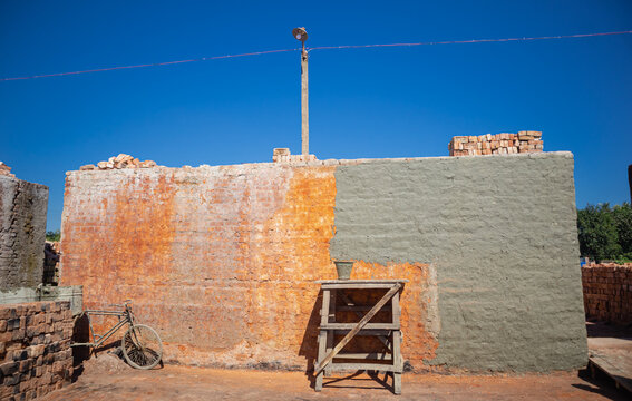 Feni, Chittagong Division, Bangladesh - 19 November 2024: View of a partially plastered brick wall at a construction site with a bicycle and wooden ladder under a clear blue sky.
