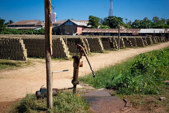 Feni, Chittagong Division, Bangladesh - 19 November 2024: View of rows of sun-dried mud bricks stacked in a brickyard with a manual water pump in the foreground.