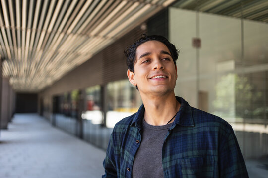 Young man portrait in outdoor modern city environment. Smiling and positive student freelancer
