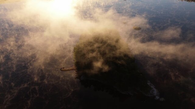 Aerial view of Finnsjon lake with a small island shrouded in morning mist under golden sunlight in Molnlycke, Vastra Gotalands lan, Sweden.