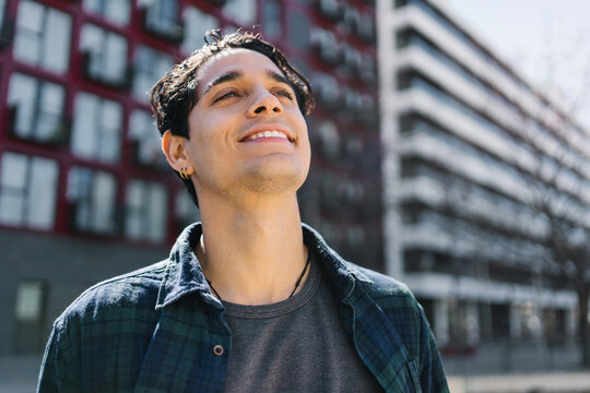 Young confident smiling student portrait outdoors looking upward near modern university campus buildings