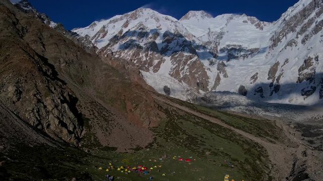Aerial view of the Diamir face of Nanga Parbat with a mountaineering base camp featuring colorful tents nestled in the rugged mountain valley, Diamir, Gilgit Baltistan, Pakistan.